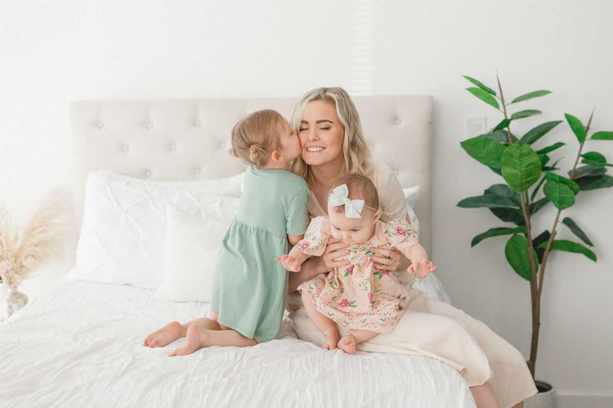 mom snuggling her babies on a white bed for mommy and me mini session az