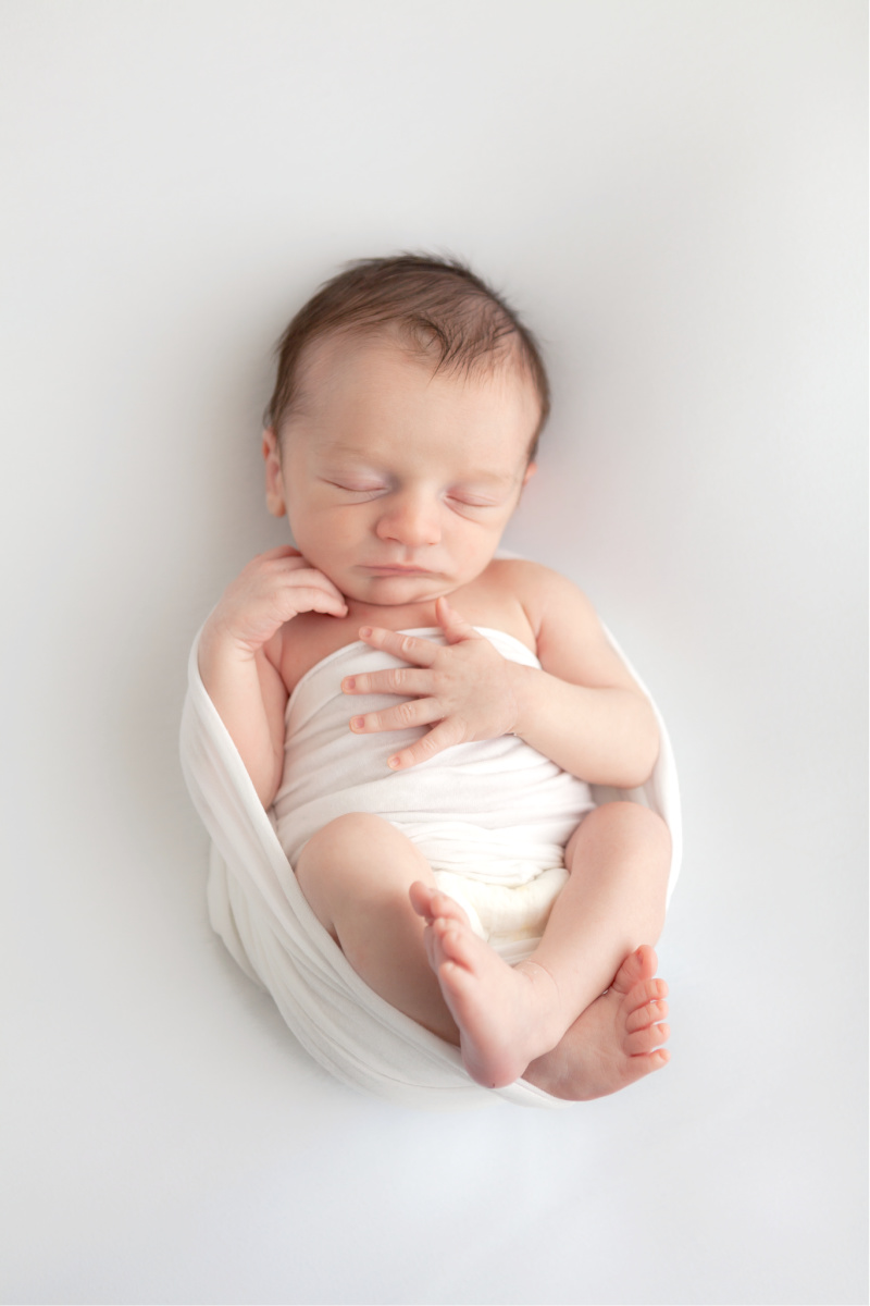 Baby boy in studio photo session. Sleeping on a white background wrapped in white swaddle.