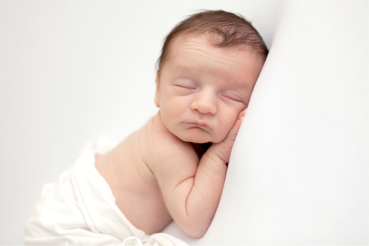 Newborn boy sleeping on his tummy with his hand under his cheek. Studio newborn session.