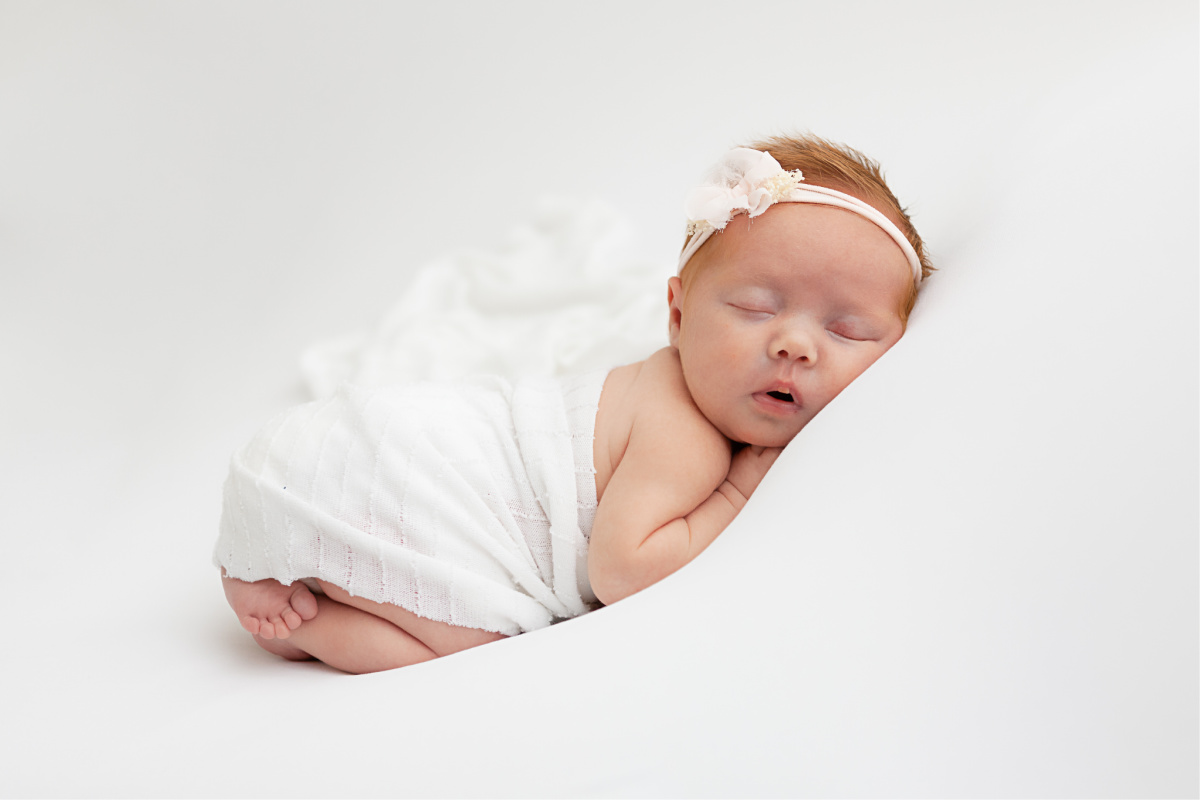 Newborn baby girl laying on her tummy. On a white background in a studio newborn session.