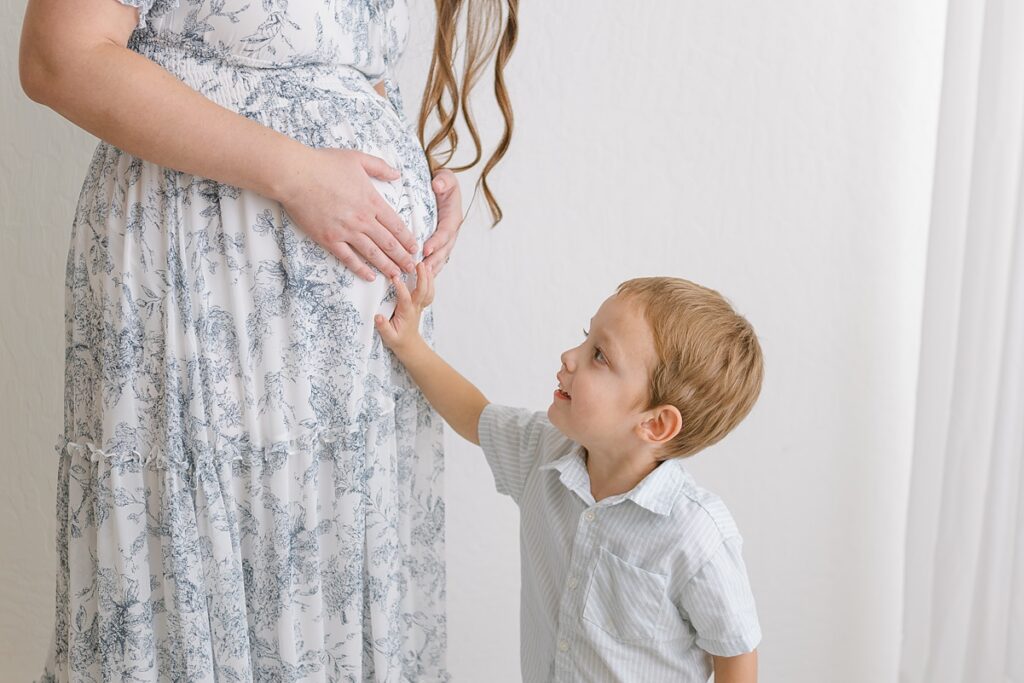 Toddler son putting his hand on mom's pregnant belly in a studio maternity session in mesa arizona.