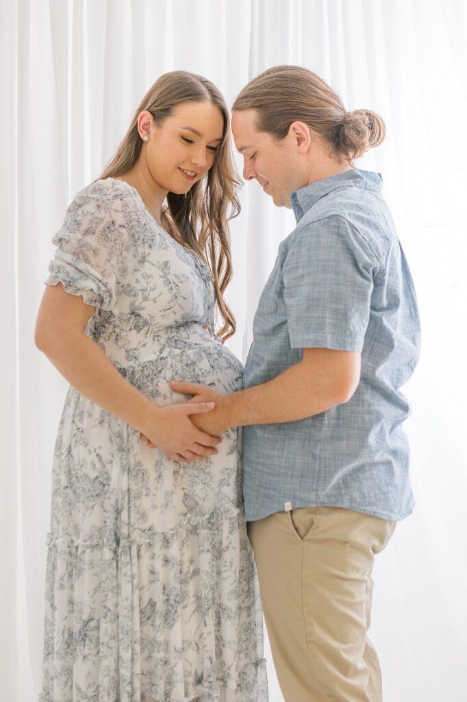 Expecting mom and dad facing each other with dad's hands on her pregnant belly. 