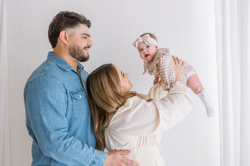 parents holding 6 month old baby girl in the air in mesa photo studio