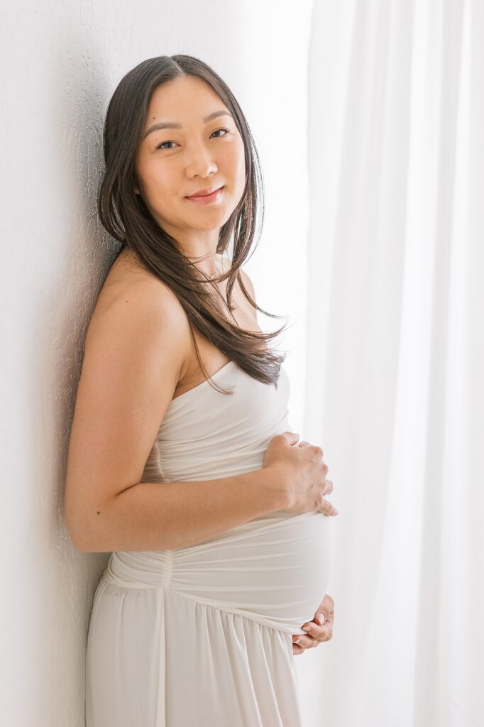 maternity photo of an asian woman in body hugging white dress in photo studio in mesa arizona