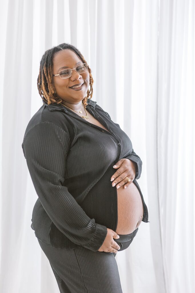 pregnant african american woman in black outfit in front of a white curtain for her maternity photo in mesa arizona