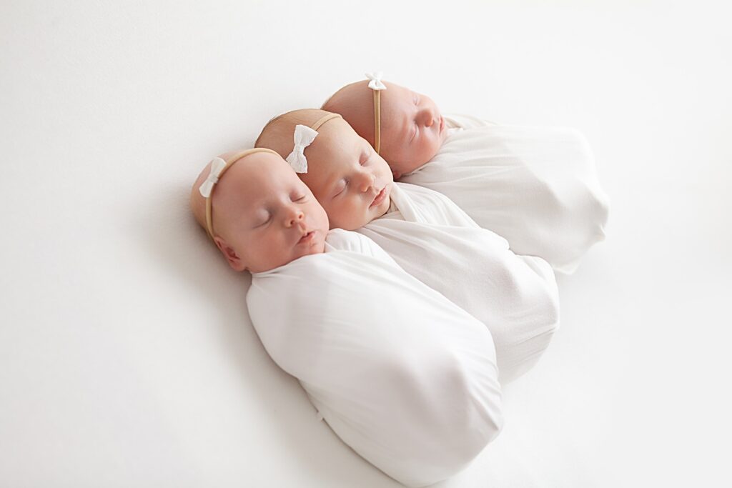newborn triplets wrapped in white swaddles laying on white backdrop in phoenix photo studio