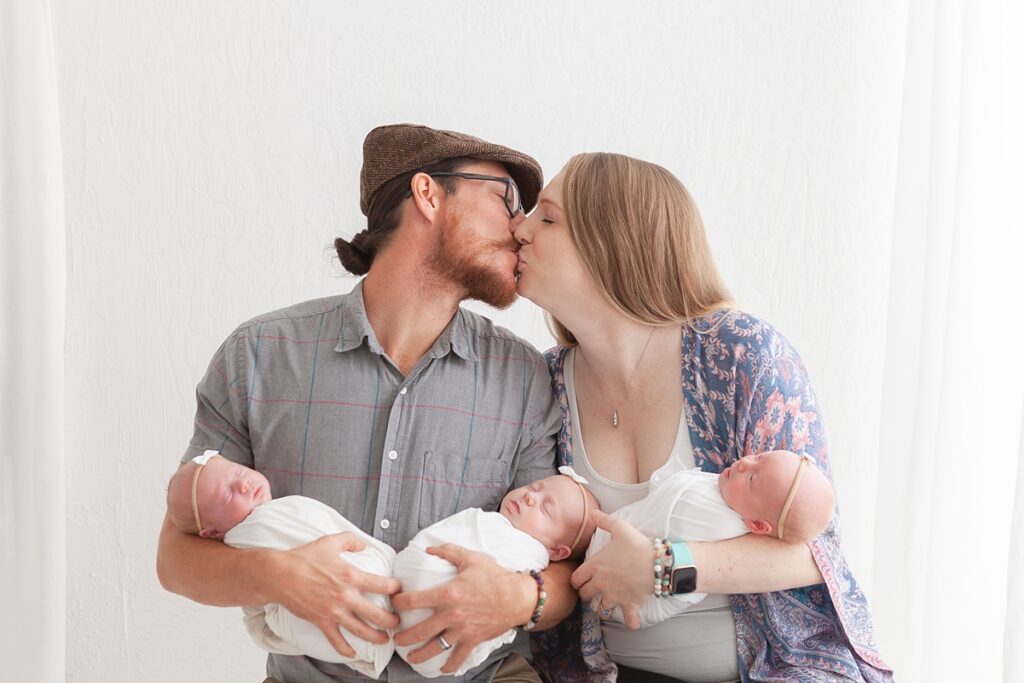 parents holding newborn triplets and sharing a kiss in phoenix arizona photography studio