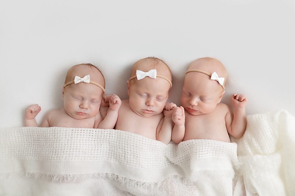 newborn triplets laying side by side under white blanket in phoenix studio