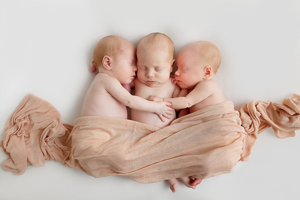newborn triplet baby girls cuddling on white backdrop in phoenix arizona photography studio sally whetten photography