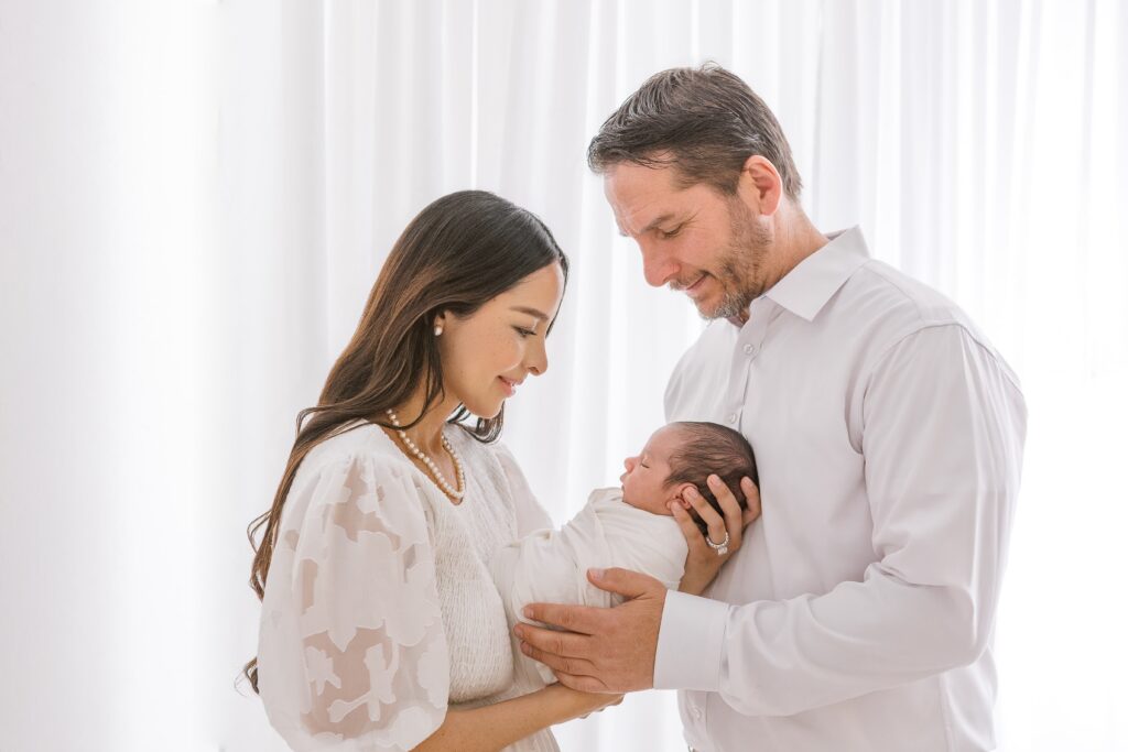 Mom in a beautiful white dress and dad in white shirt holding baby boy in scottsdale newborn photography studio