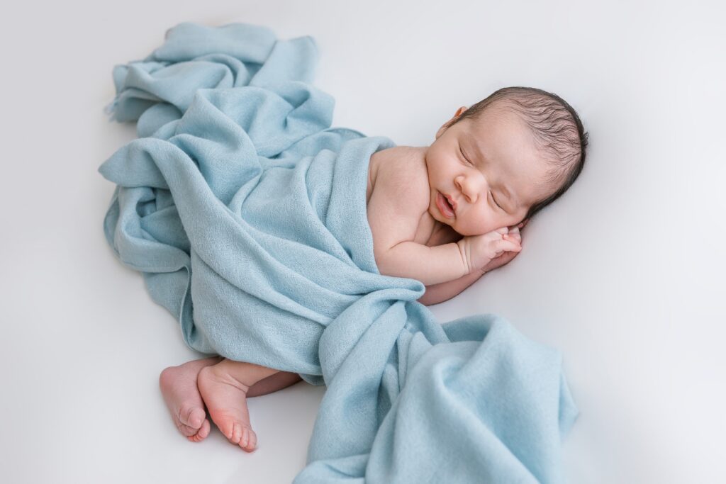Scottsdale newborn photographer Sally Whetten photographed this newborn baby boy sleeping in a light blue blanket on a white backdrop.