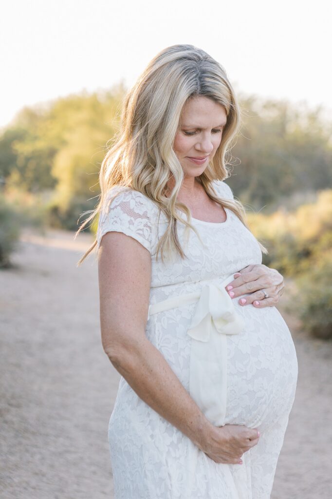 Beautiful pregnant mom cradling her belly with her arms, looking at her belly in the Phoenix desert at sunset.
