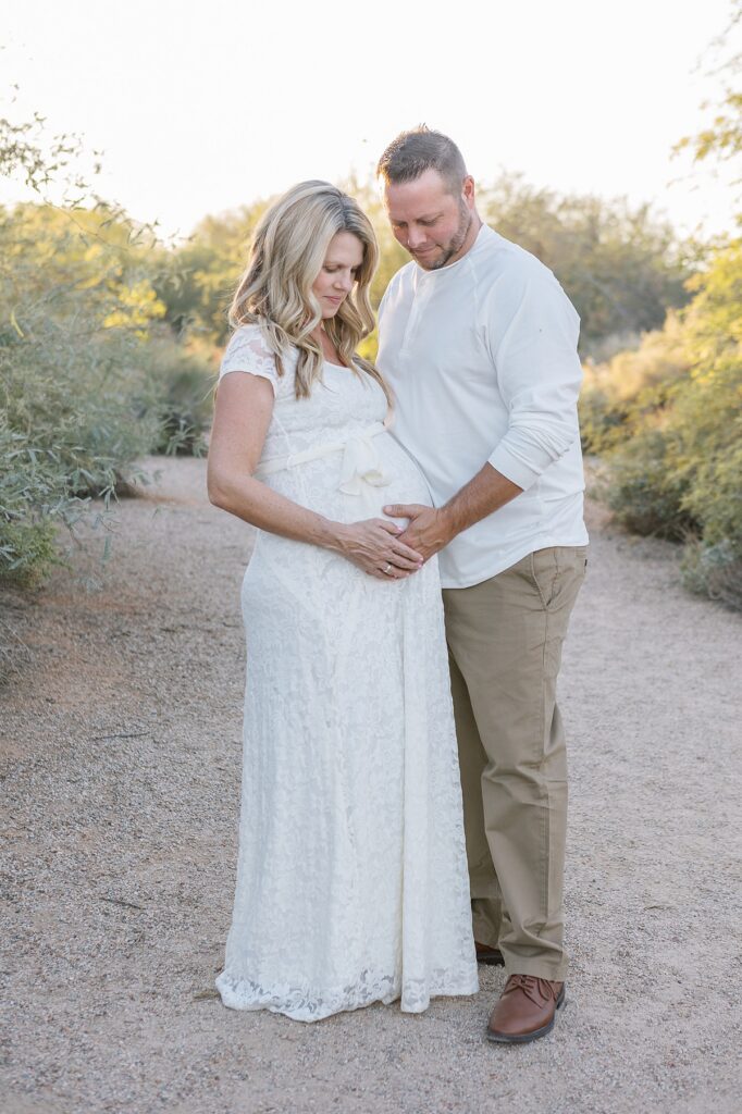 husband and wife looking at her pregnant belly in lovely golden light in phoenix
