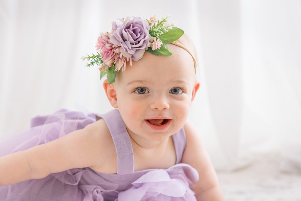 smiling baby girl crawling in a purple dress with flower headband that matches