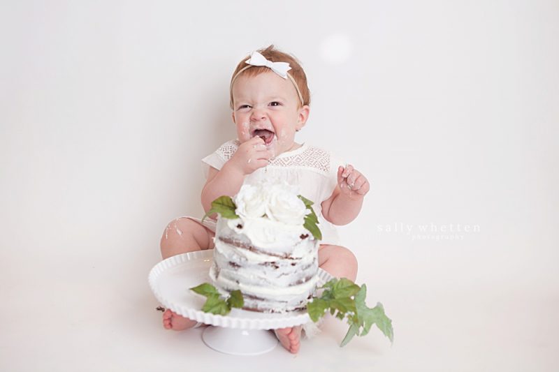 one year old smashing cake and smiling in white photo studio