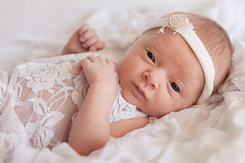 Sweet newborn baby girl wearing white lace romper with cute white headband