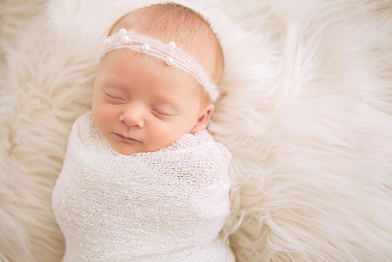 Beautiful newborn baby girl wearing delicate pearl headband sleeping on white fur