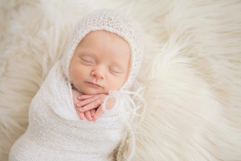 sleeping newborn baby girl wearing white bonnet lying on a white fur blanket