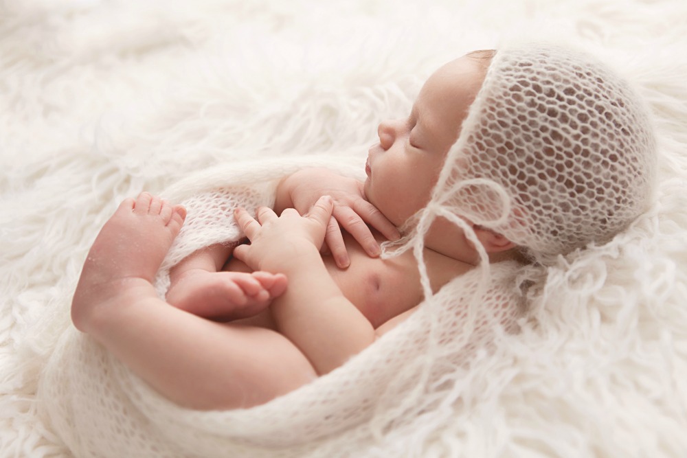 sweet baby girl in knit bonnet laying on white fur blanket