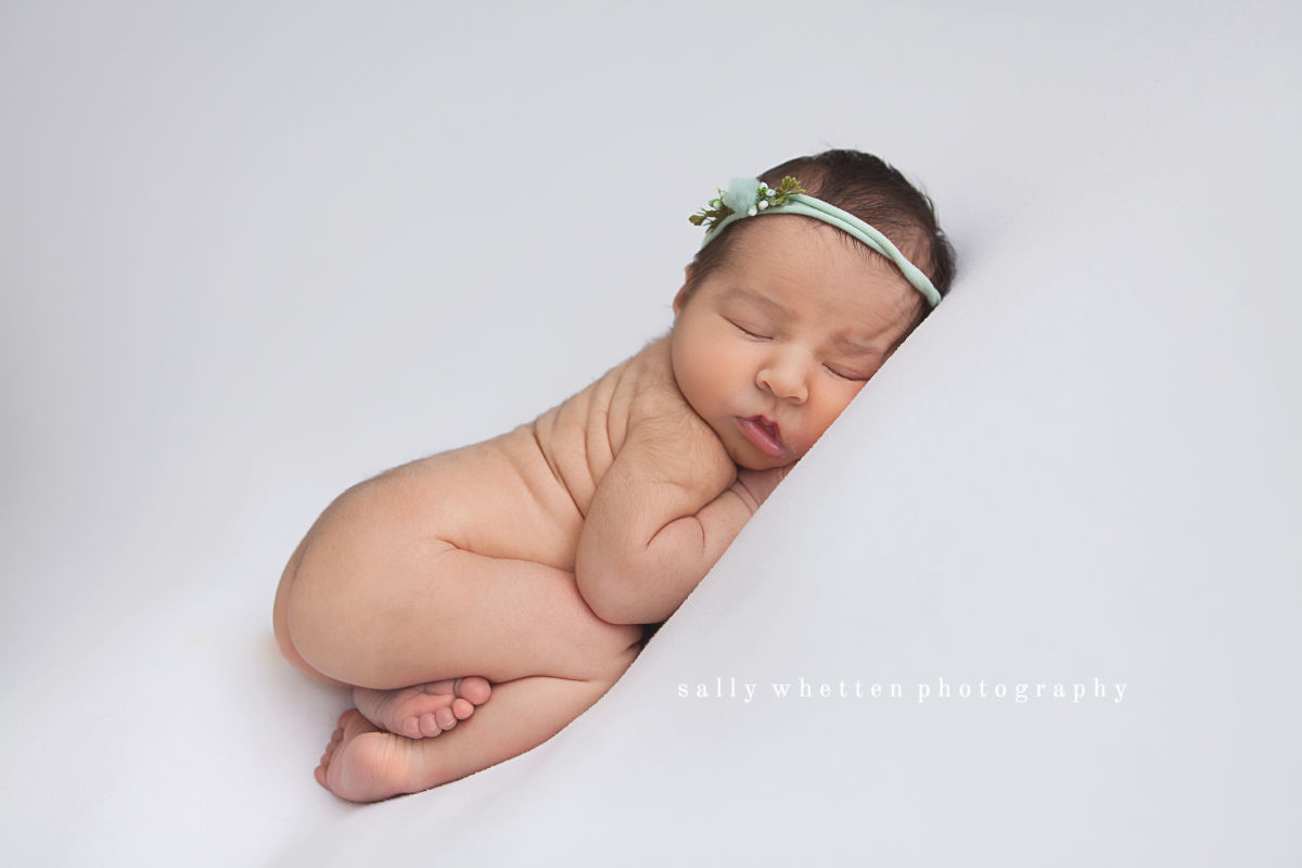 baby curled up on white blanket with delicate green headband