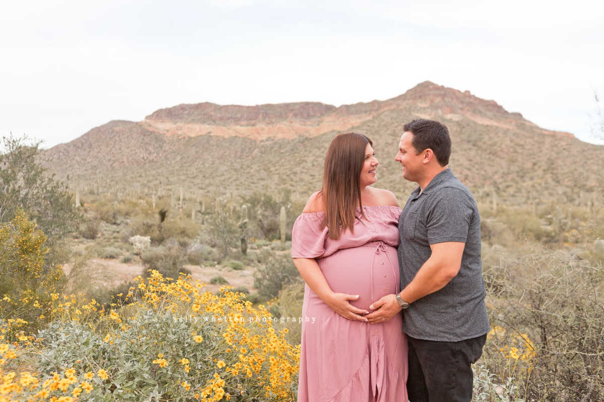 couple posing for maternity photos by wildflowers in the desert 