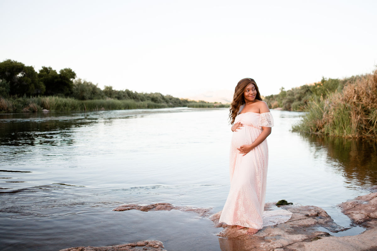 pregnant woman of color by the river in long pink lace gown
