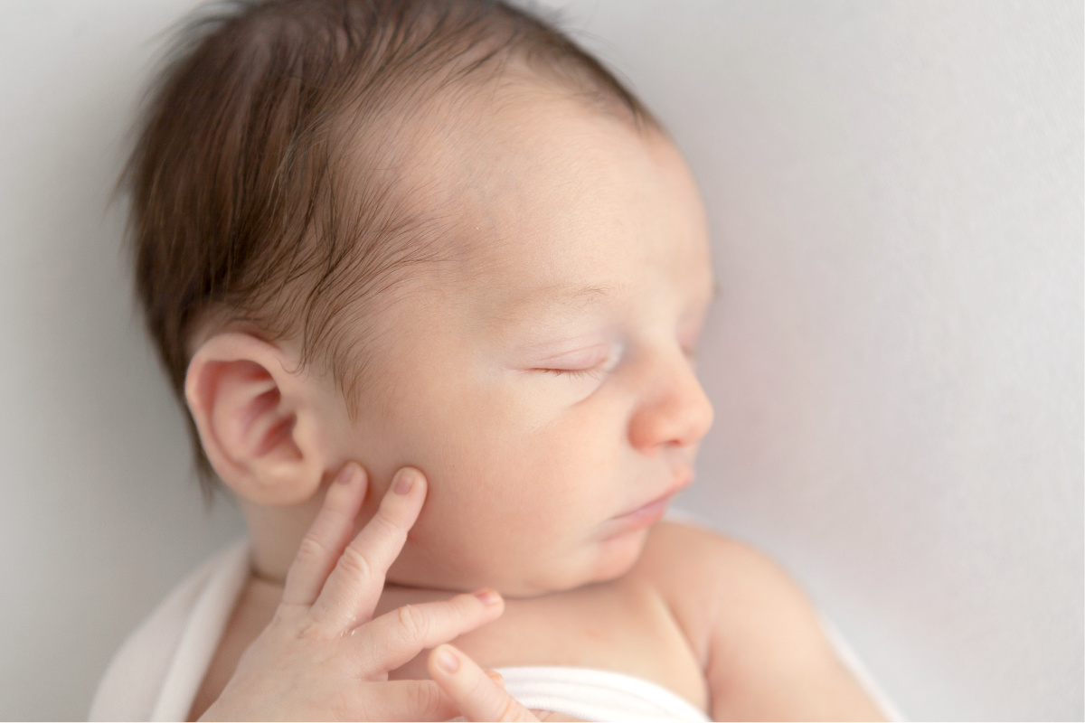 Close up profile of newborn baby boy. Sleeping on a white background with fingers on his cheek.