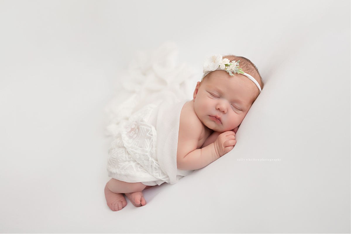 Newborn baby girl swaddled in a white blanket. Photographed in a studio with a white backdrop, by award winning photographer Sally Whetten.