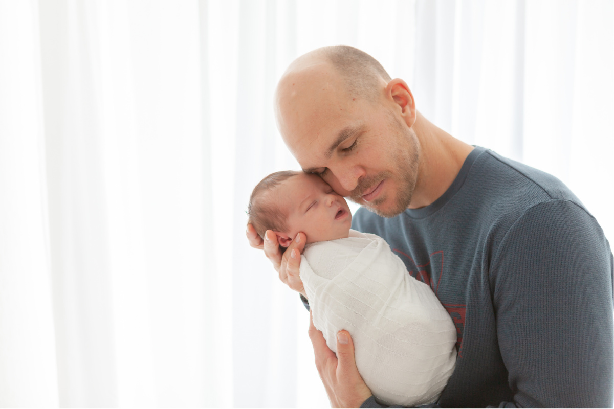 Dad in a white studio holding newborn son with eyes closed