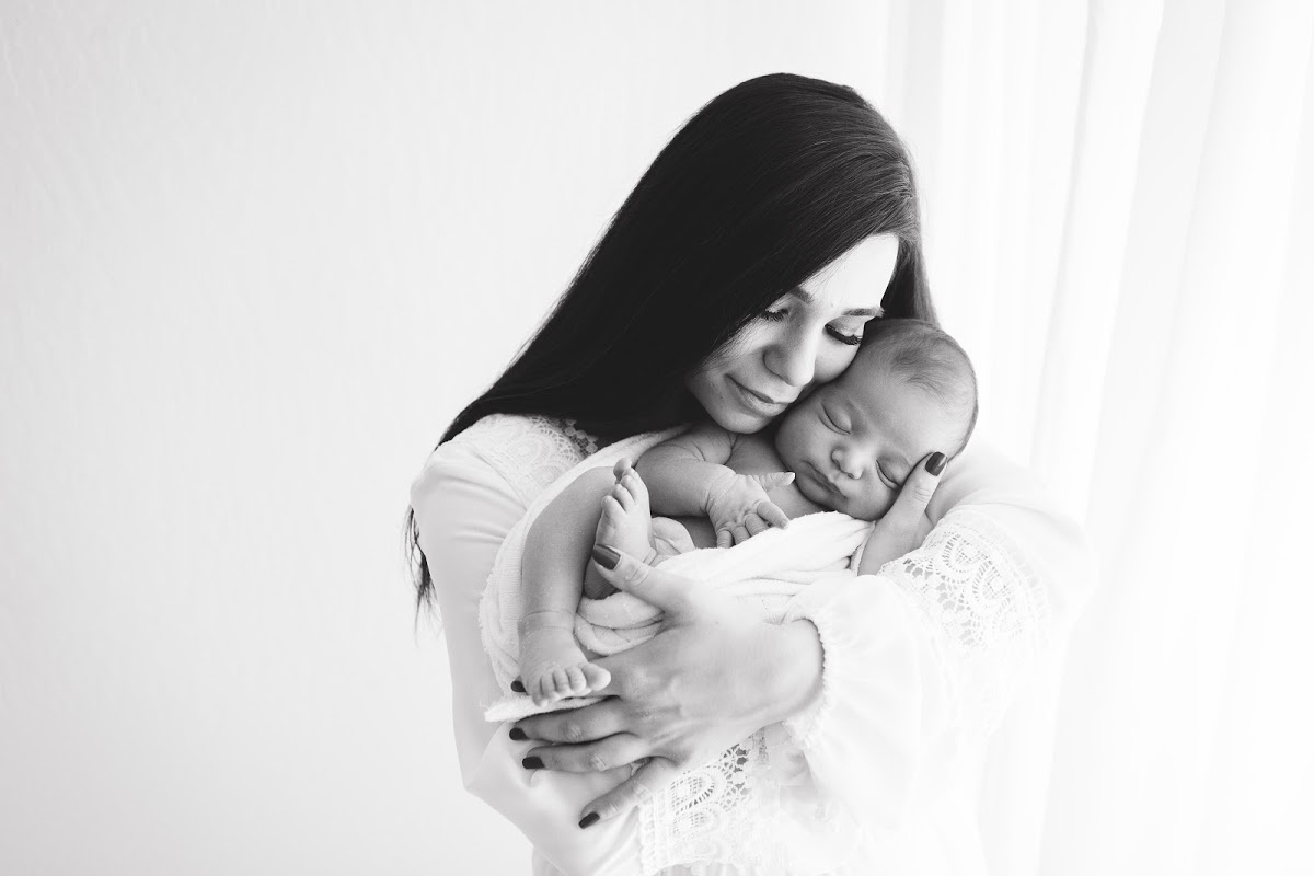 black and white picture of mom cradling newborn son in white studio