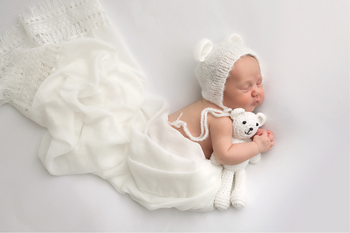 Scottsdale Newborn Photographer newborn baby girl in white bonnet holding white teddy bear sleeping with white blanket
