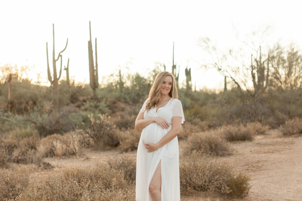 Pregnant woman in white dress in beautiful desert landscape