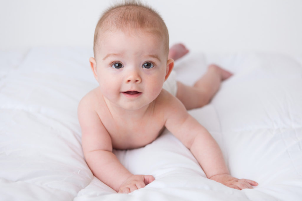 6 month old baby boy laying on his tummy for his photo session on a white blanket.