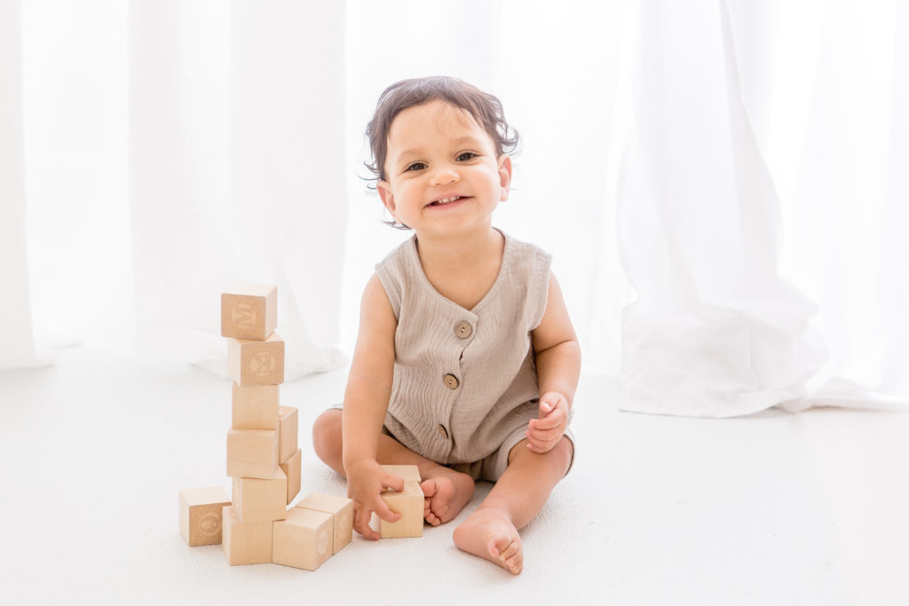 one year old boy sitting and smiling while playing with blocks at his one year photo session
