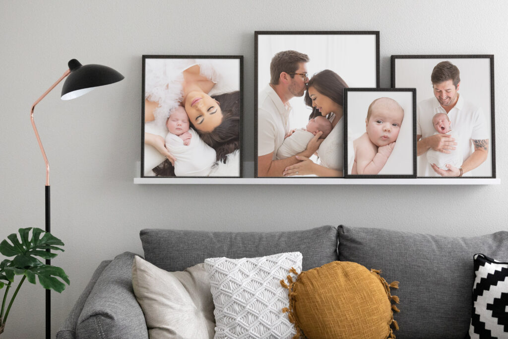 Modern living room with gray couch and white picture ledge. Four newborn family pictures sit on the ledge in slim black frames. Beautiful newborn portraits with white backgrounds by Sally Whetten Photography.