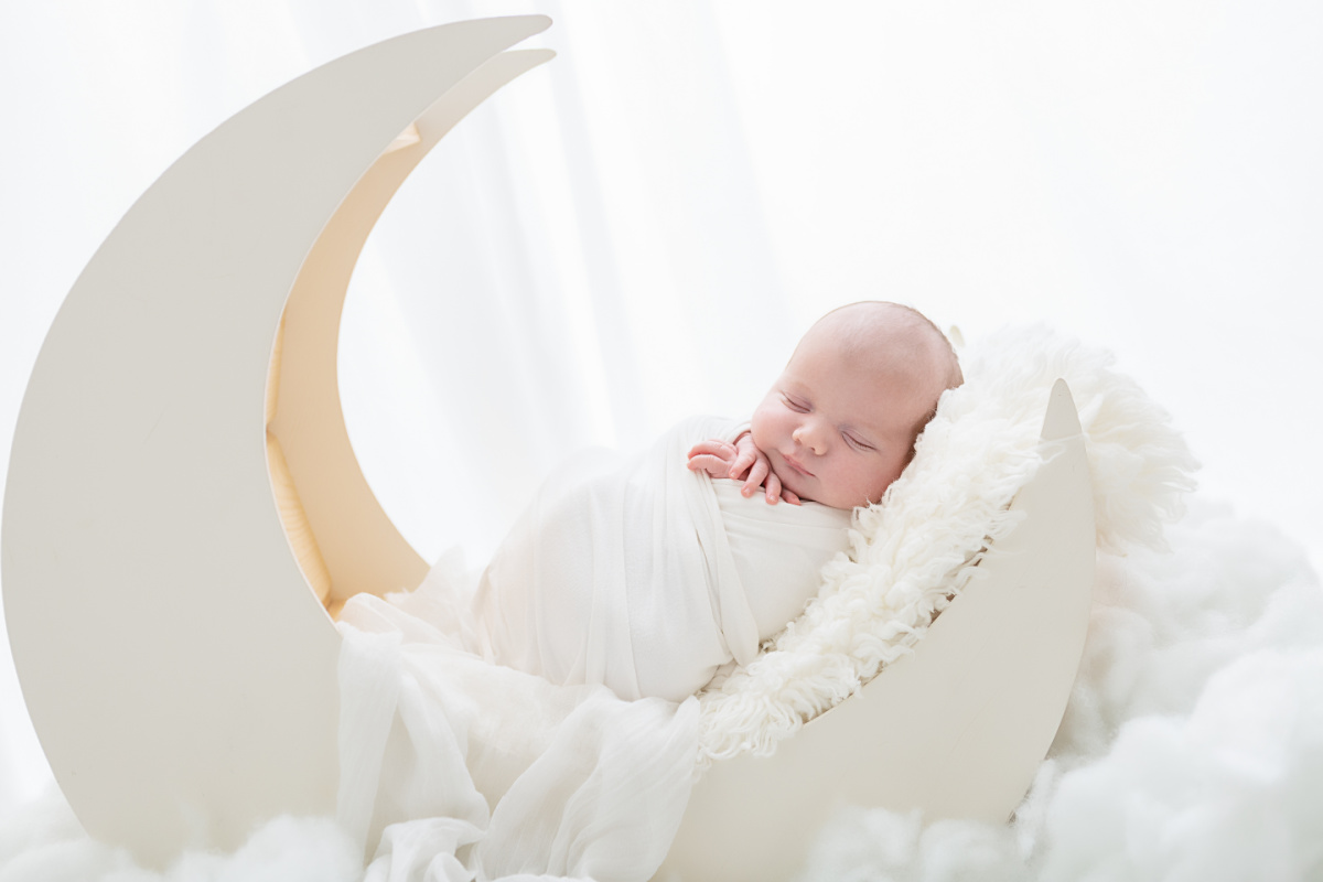 Newborn baby boy sleeping peacefully in moon photography prop, in the Sally Whetten Photography studio.