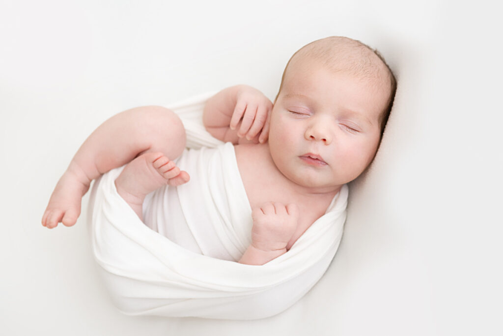 Newborn baby boy wrapped in a white swaddle, sleeping on a white background in Mesa Newborn Photographer Sally Whetten Photography studio. 