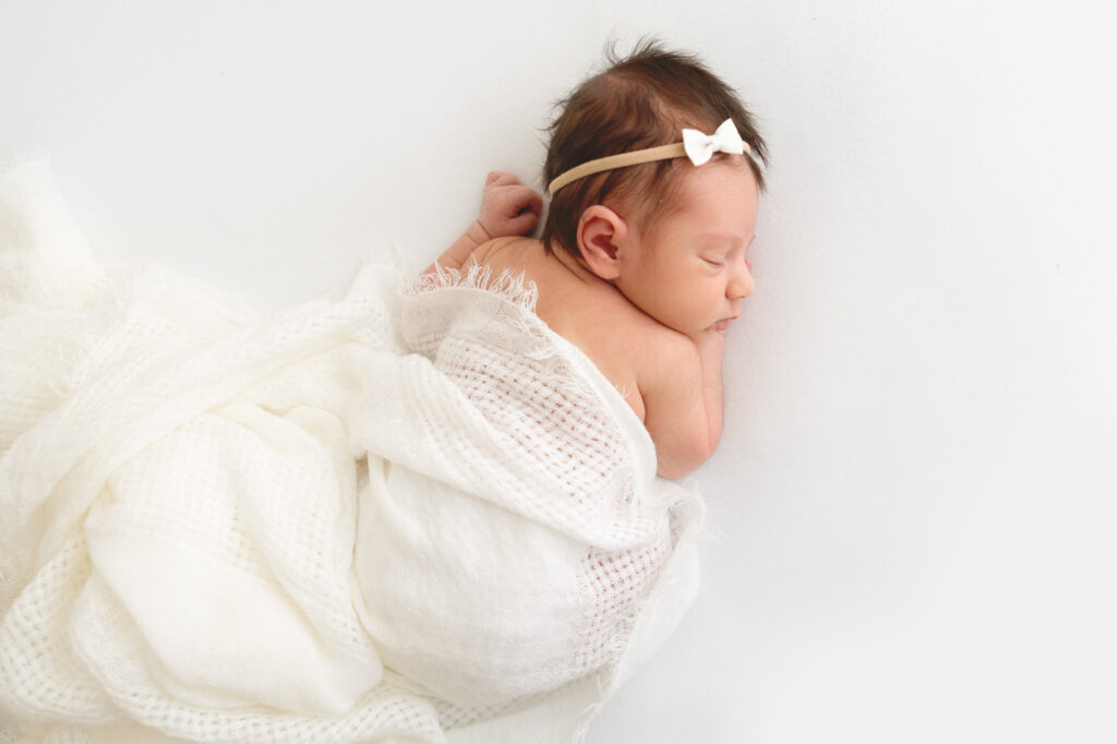 Newborn baby sleeping on her tummy with a white blanket in studio newborn session in Phoenix.