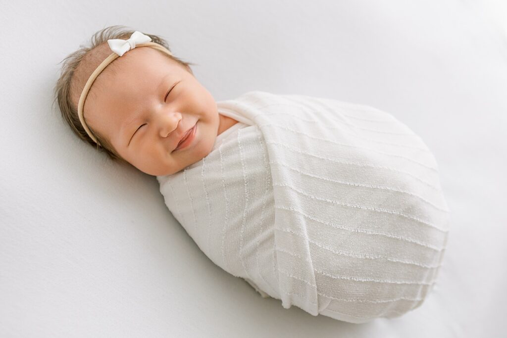 Best newborn photographer Scottsdale captures a peaceful studio portrait of a baby girl swaddled on a cozy white blanket.