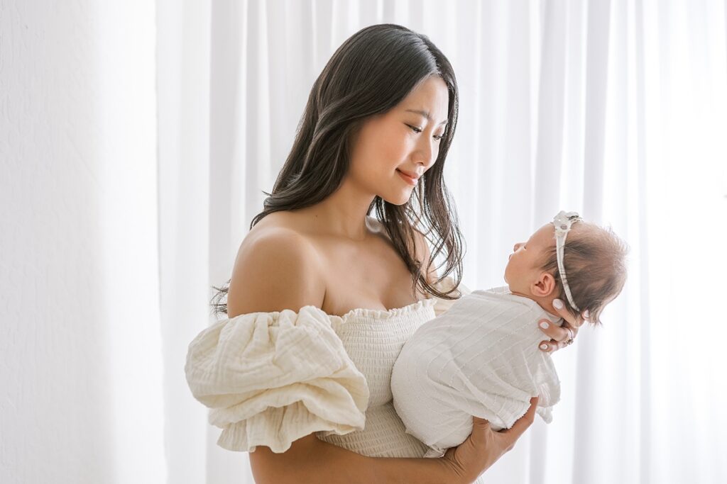 Best newborn photographer Scottsdale documents a soft, emotional portrait of mom cuddling her baby girl in a peaceful studio setting.