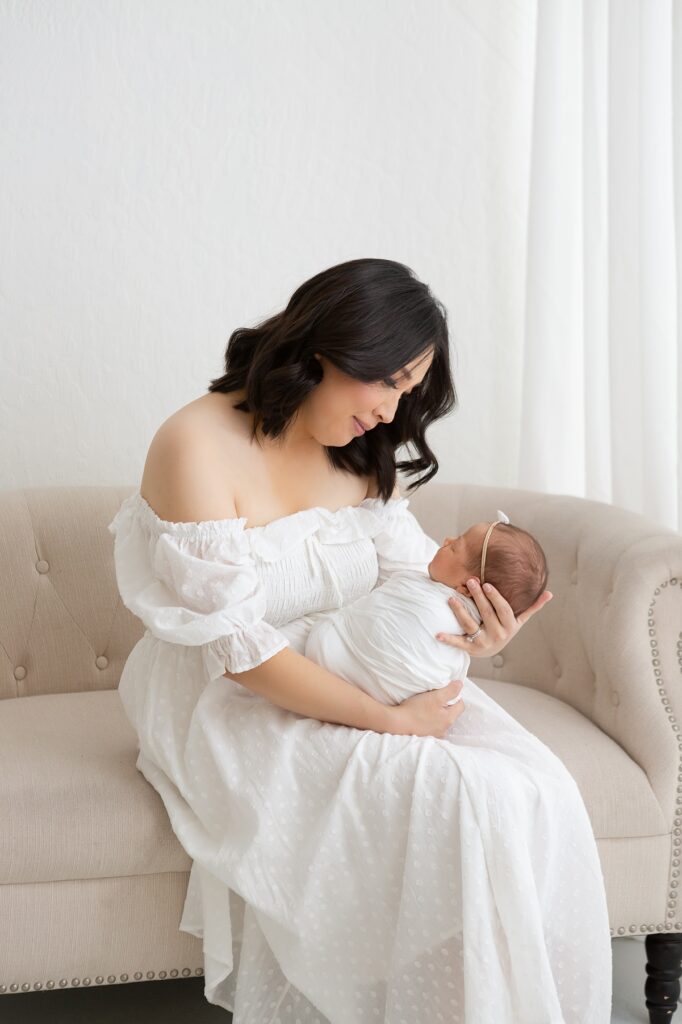 a soft, natural moment of a mother holding her baby in a bright white studio setting.