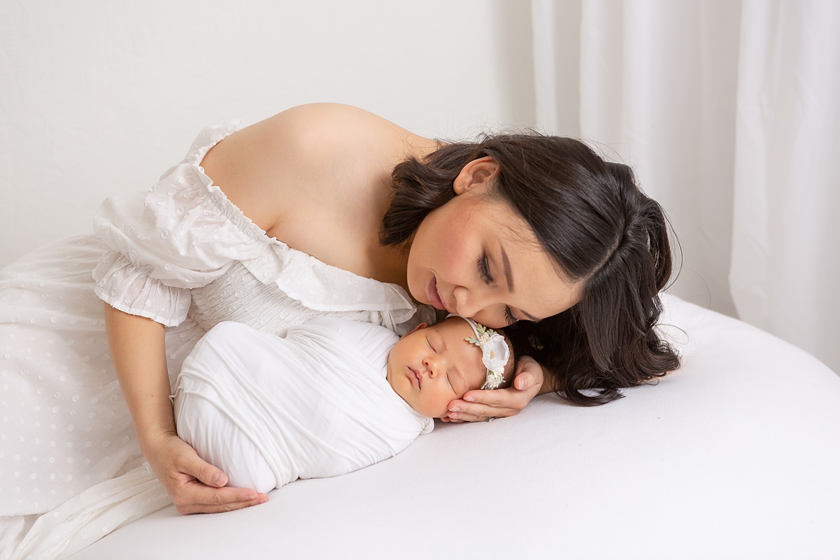 Phoenix baby photographer captures a tender moment of a mother lying with her newborn on a white blanket, soaking in the quiet closeness of early motherhood.