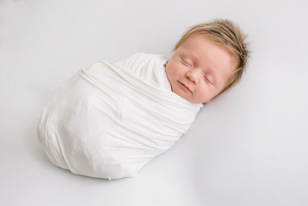 Sleeping newborn baby boy with a full head of light hair, resting peacefully on a soft surface.