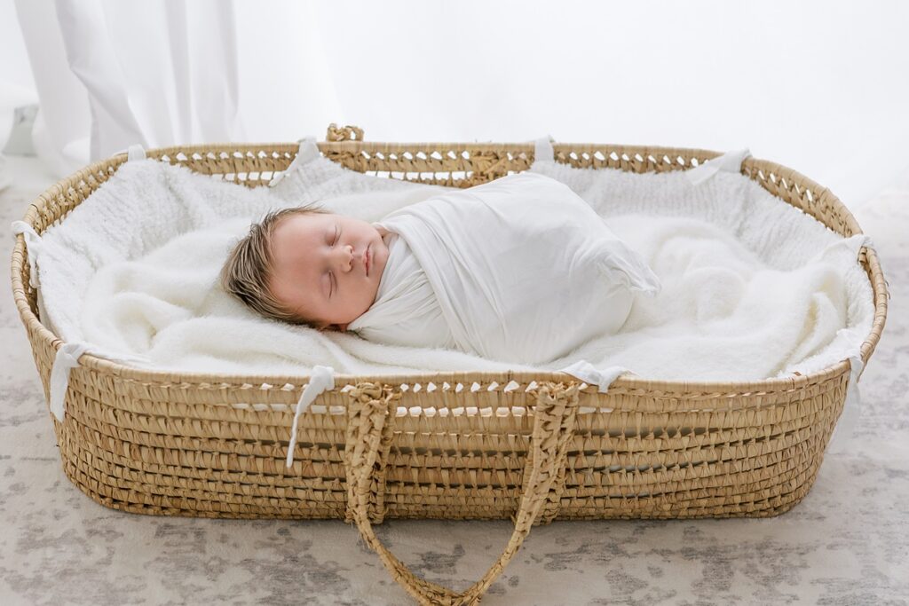 Newborn baby boy lying in a woven Moses basket, wrapped in a light blanket.