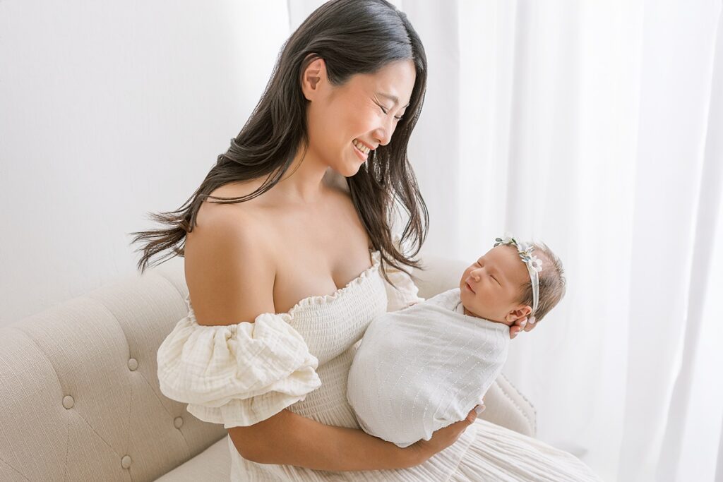 Postpartum mom wearing soft neutral dress, smiling down at baby
