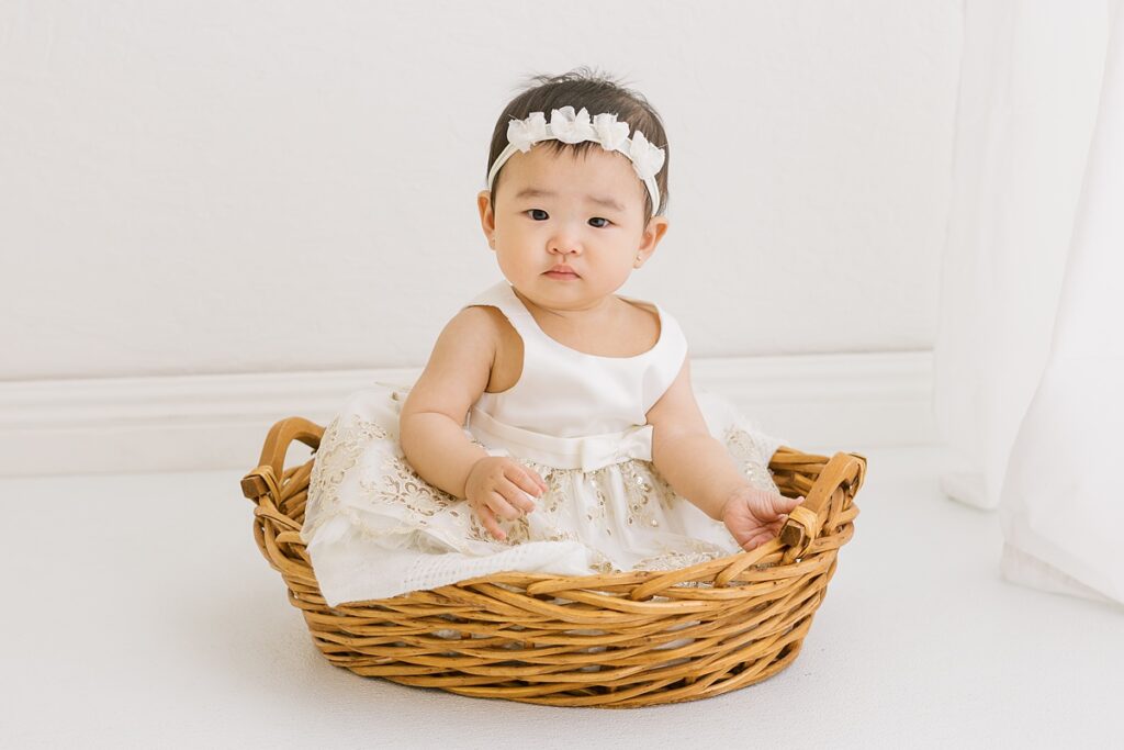 Baby girl sitting in woven basket during light and airy studio sitter session