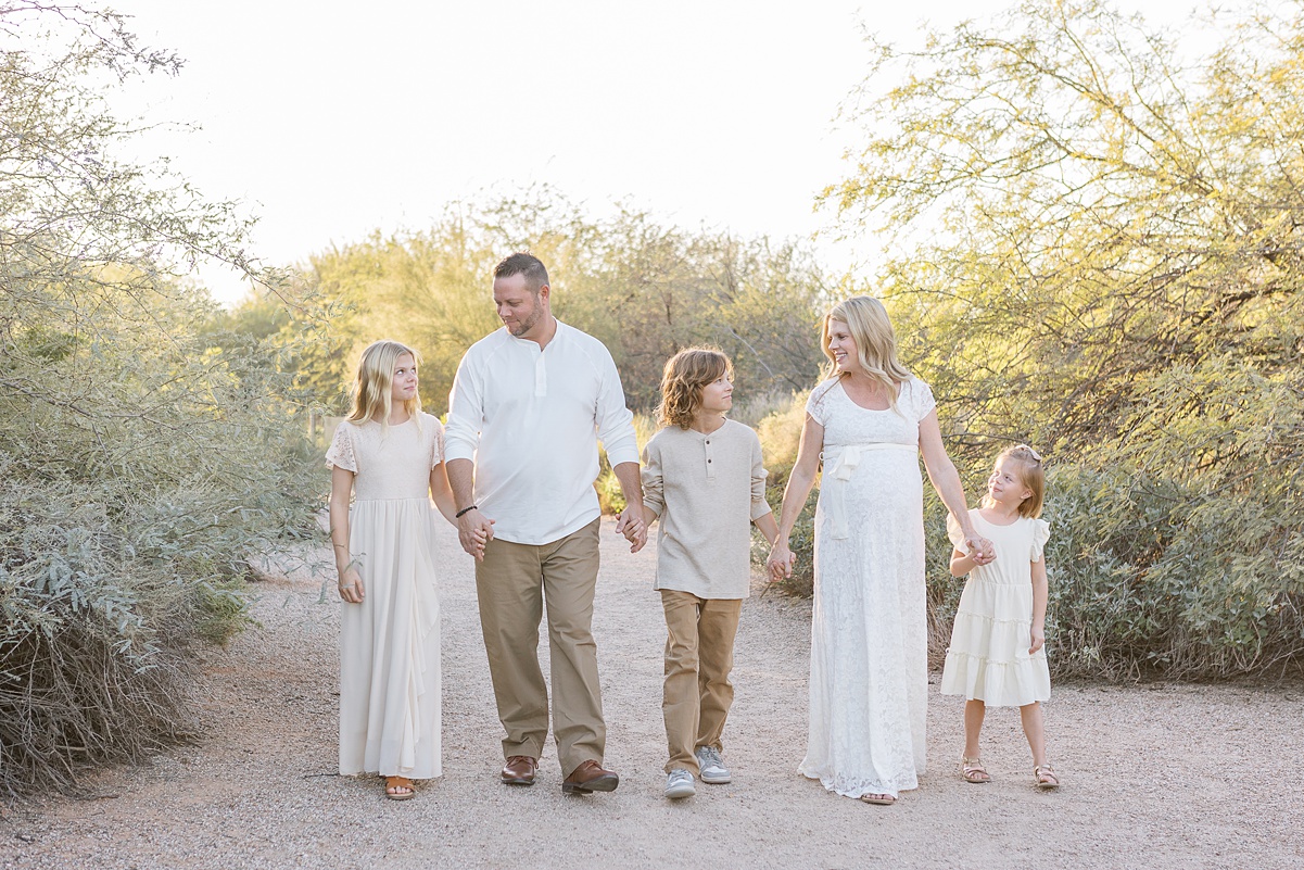 Family of 5 in neutral clothes holding hands in a line and walking in beautiful desert in the evening.