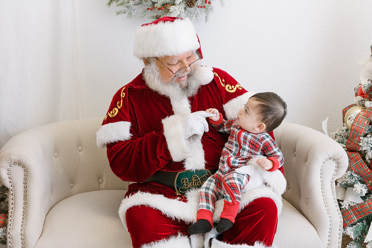 one year old boy sitting on santa's lap, looking at him.